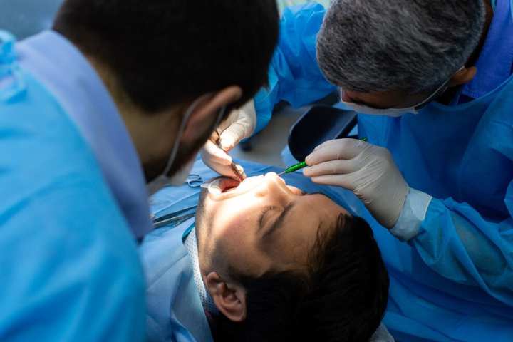 maxilofacial que es: dos médicos examinando la boca de un paciente